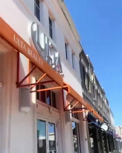 Fachada de una tienda de belleza con toldo naranja en una calle comercial